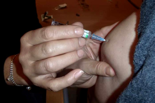 Kädet laittavat rokotusneulan potilaan käsivarteen.