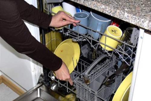 Ihminen tyhjentää astioita pesukoneesta.