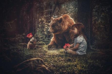 Valokuvassa on satumainen maisema, jossa on pieni tyttö ja karhu.
