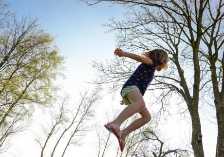Valokuvassa tyttö hyppii trampoliinilla ulkona.