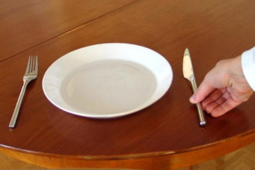 Käsi laittaa veitsen pöydälle lautasen viereen.