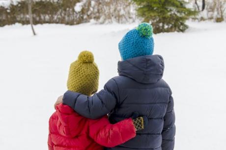 kaksi lasta seisoo selin talvisessa maisemassa käsi toistensa hartialla tai selässä
